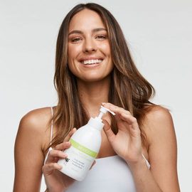 Smiling brunette female holding 500ml MooGoo Cream conditioner bottle. 