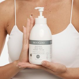 A female model wearing white singlet top holding the MooGoo Natural Skin Milk Udder Cream in front of her chest with both hands. 